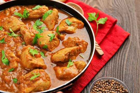 Tasty chicken curry in pan and spices on wooden background