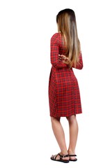 back view of standing young beautiful woman. girl watching. girl in red plaid dress standing sideways with his arms crossed behind his back.