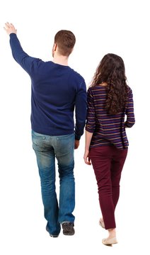 Back view of walking young couple (man and woman) pointing. Rear view people collection. Swarthy girl and the bearded man on the move shows his hands up.
