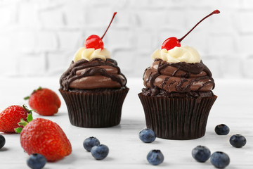 Delicious chocolate cupcakes with berries on white table