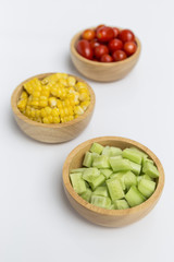 Fresh cucumber, sweet corn, tomato in round wooden bowl on white background