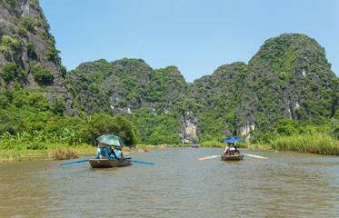 Fototapeta na wymiar Tourists asia traveling in boat along nature the river and mountain. at Tam Coc portion, Ninh Binh Province, Vietnam. Rower using her feet to propel oars. landscape river and mountain