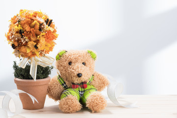 cute teddy bear sitting at side of dry flowerpot with ribbon on wood