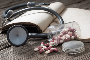 still life photography : old capsule spill from container with stethoscope and old textbook on old...