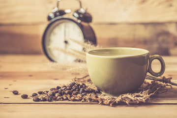 aroma hot black coffee or Americano and Arabica coffee bean with smoke and vintage clock on wood background, wake up morning time with coffee concept.