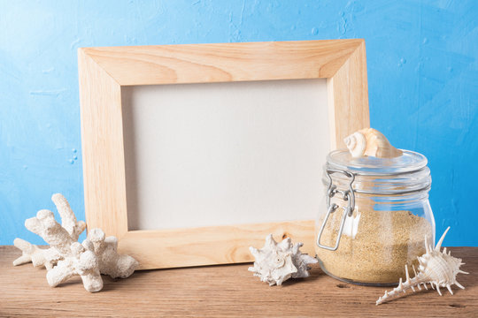 still life photography : handicraft wood frame with sand in glass jar, shell and coral on blue texture background in sea element concept