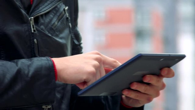 young man stands and works on tablet on urban street in front of modern building in the city - closeup hands