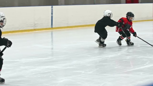 Slow motion tracking of little ice hockey player stealing puck and trying to score goal while novice defenseman body checking opposite teams forward