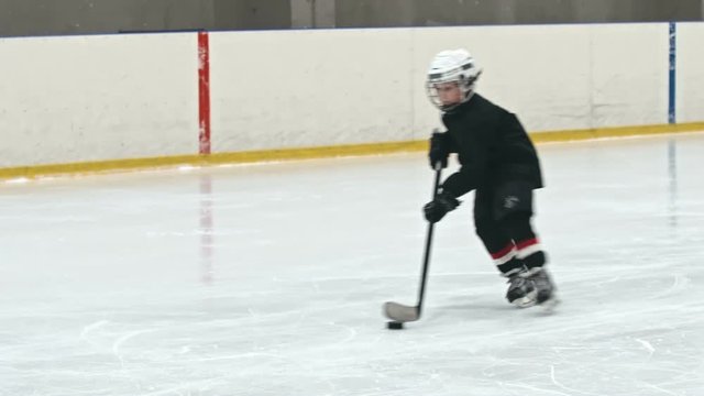 Slow motion tracking of novice forward player hitting puck towards opposing teams net and failing to score as little goalie making save with butterfly technique
