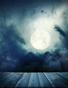 Halloween background. Spooky forest with full moon and wooden table, over light 