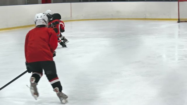 Slow motion tracking of novice grinder dribbling puck as little defenseman from opposing team body checking and trying to outrun him 