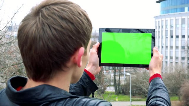 young man stands and works on tablet in park in city - green screen 