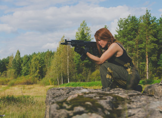 redhead girl stands on one knee and aim from the weapon.