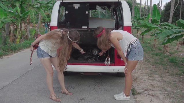 Hippie Girls Looking at Parts under the Hood of a Minivan while Standing on the Road in a Palm Grove. Slow Motion