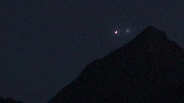 cgi compositing showing two bright glowing lights dancing in the night sky near a mountaintop