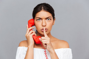 Woman talking on the phone tube and showing silence gesture