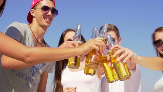 Five joyful handsome friends drinks cider at beach