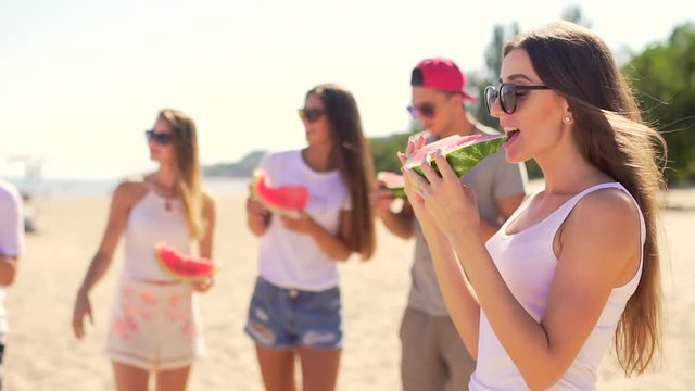 Handsome young woman eating watermelon. Friends at background