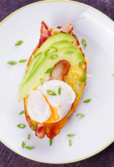 Stuffed potato with bacon, poached egg, avocado, cheese and spring onion. View from above, top studio shot