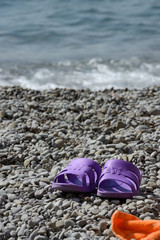 Purple beach sandals are on the grey pebble in sunlight.