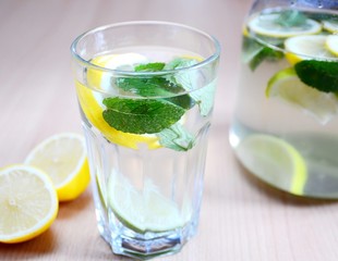 Fresh non-alcoholic drink with water mint leaves peaces of lemons and limes in glass.