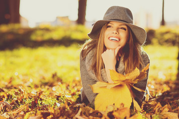 Happy young blonde woman in park in autumn holding leaves