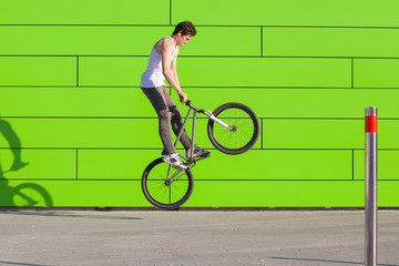 Boy on bike make the bunny hop trick at green wall background
