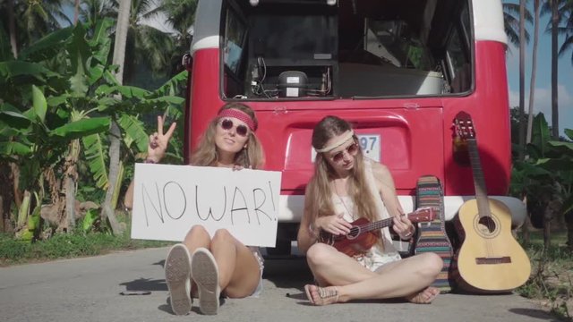 Hippie Girls Sitting on a Road with a White Board with the inscription "No War". Slow Motion