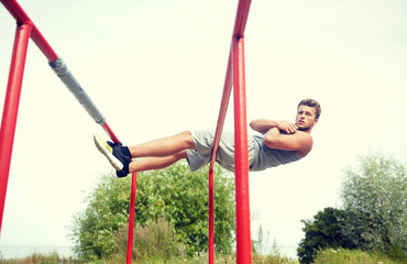 young man doing sit up on parallel bars outdoors