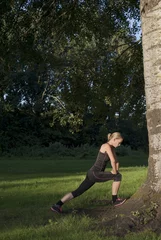 Foto op Plexiglas sportieve jonge vrouw doet rek oefeningen buiten als warming up voor hardlopen © monicaclick