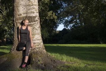 Poster knappe jonge vrouw leunt tegen boom en geniet van zon in sportkleding © monicaclick