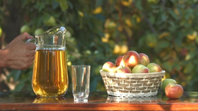 Apple juice and basket with apples on the background of growing apples. Slow motion.