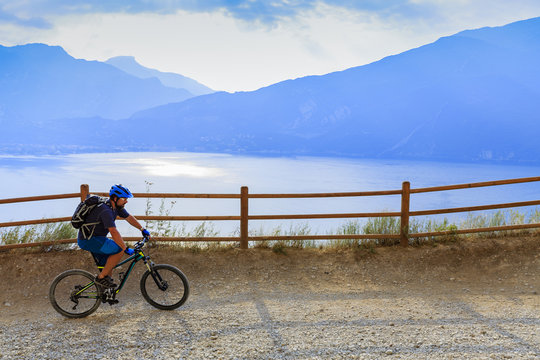 Mountain biking at sunrise man over Lake Garda on path Sentiero della Ponale, Riva del Garda, Italy