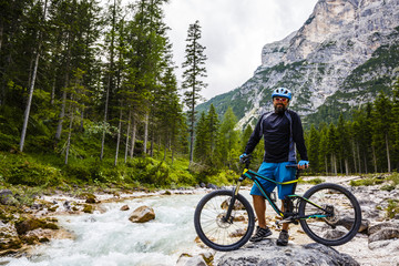 Mountain Bike cyclist standings on rocks on the banks of a mountain river, active vacation in italian Alps