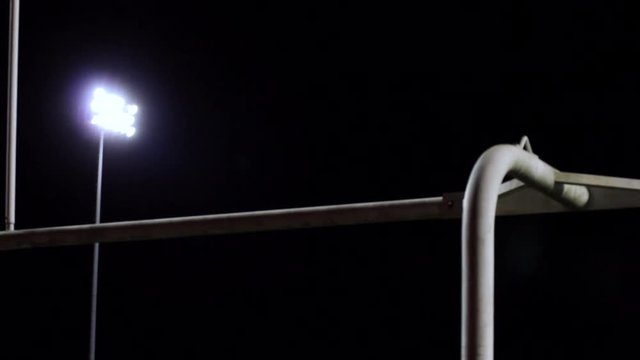 Dolly across a goalpost with a stadium light shining on a field.