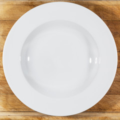 Soup deep white round plate with wide shoulders on wooden cutting board directly from above