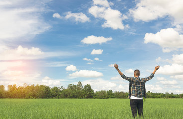 Enjoyment - free happy young man enjoying sunrise. The young man in plaid shirt  with arms outspread and face raised in sky enjoying peace, serenity in green meadow