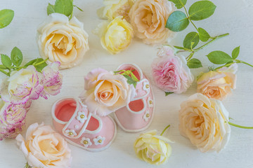 New baby card. Baby booties figurine of marshmallow,in the midst of pink roses on a white wooden background