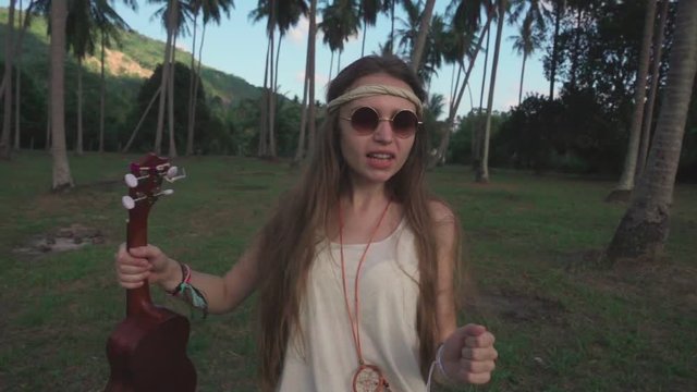Hippie Girl Having Fun Dances in a Palm Grove with an Ukulele. Slow Motion