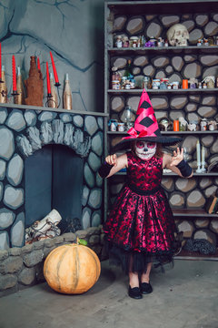 Girl in witch costume and makeup on her face standing in halloween decorations