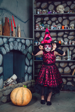 Girl in witch costume and makeup on her face standing in halloween decorations