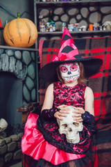Fototapeta na wymiar Girl in a witch costume sitting in chair with skull in his hands in in halloween decorations