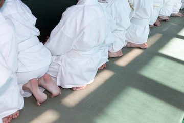 Fototapeta premium Group of children in kimono sitting on tatami on martial arts training seminar. Selective focus