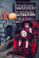 Girl in a witch costume sitting in  chair with  skull in his hands in in halloween decorations