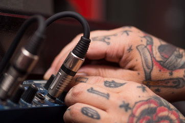 Closeup of hands covered with tattoos working on cable connection hardware audio box, studio equipment concept