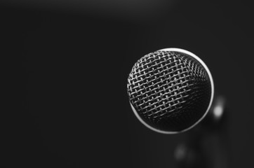 Closeup black vocal microphone mounted on mic stand, blurry red dark bcakground