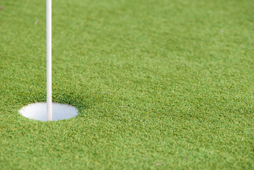 Close-up detail of a golf hole with a flagpole on artificial turf. Sports and recreation concept.