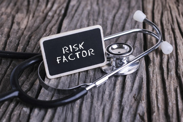 Medicine concept. Blackboard with word RISK FACTOR  and stethoscope on wooden background