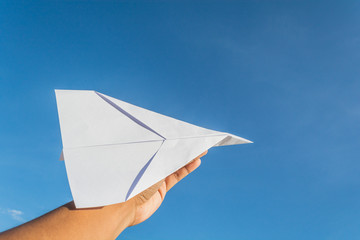 Hand holding white paper plane in bright blue sky.