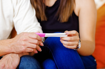 Couple seated down, holding pregnancy home test between them, pregnant concept